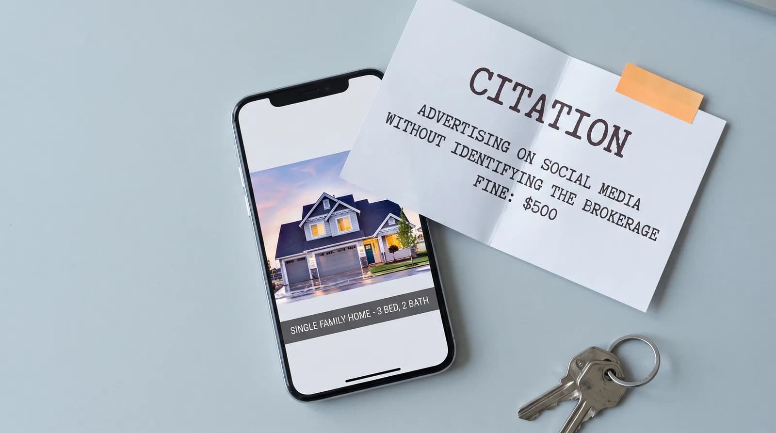 A phone on a pale blue desk showing a real estate listing post captioned single family home, 3 bed, 2 bath with no brokerage name on it, beside a printed citation notice reading advertising on social media without identifying the brokerage, fine $500, with house keys alongside